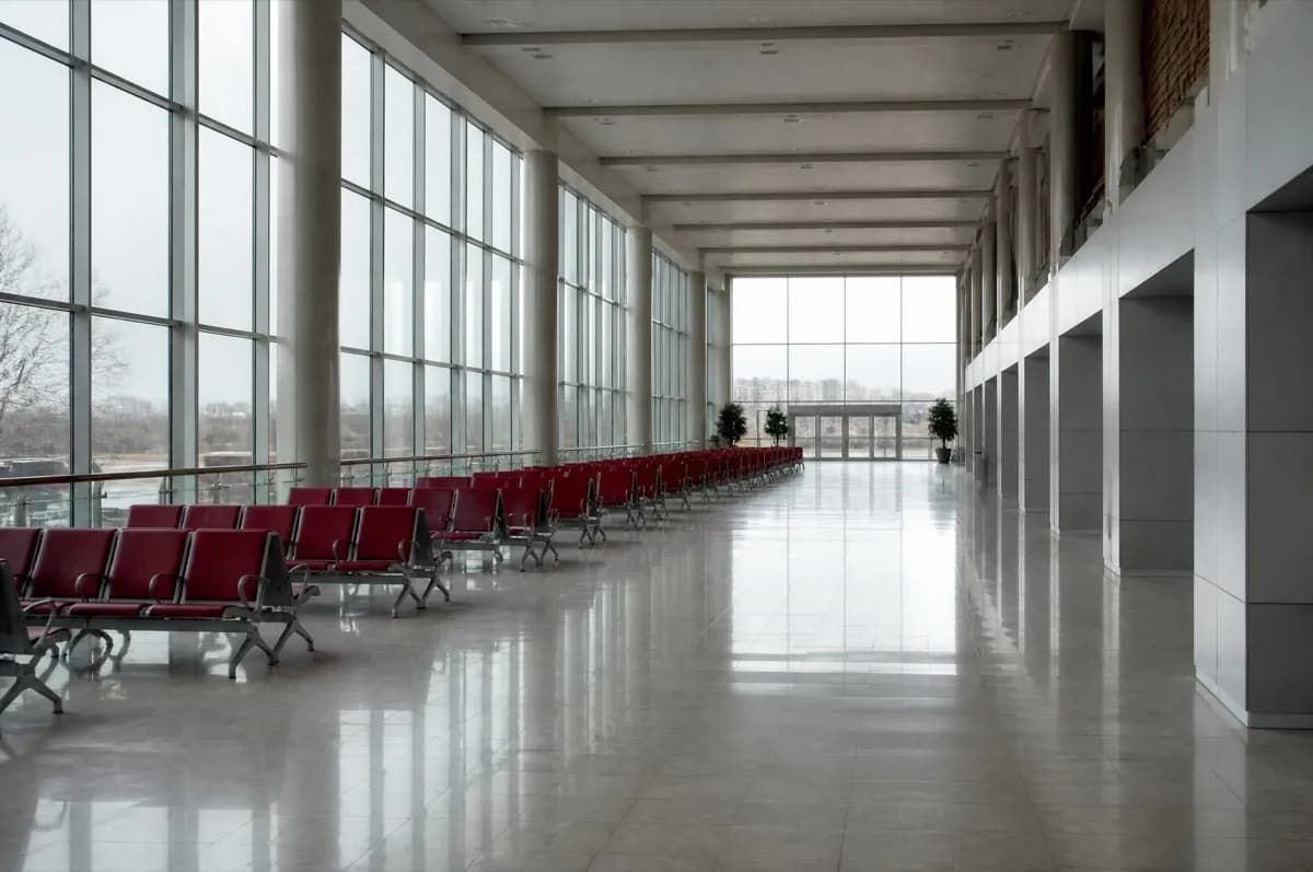 Camlı cephesi boydan boya uzanan boş terminal salonu; solda sıra sıra kırmızı bekleme koltukları